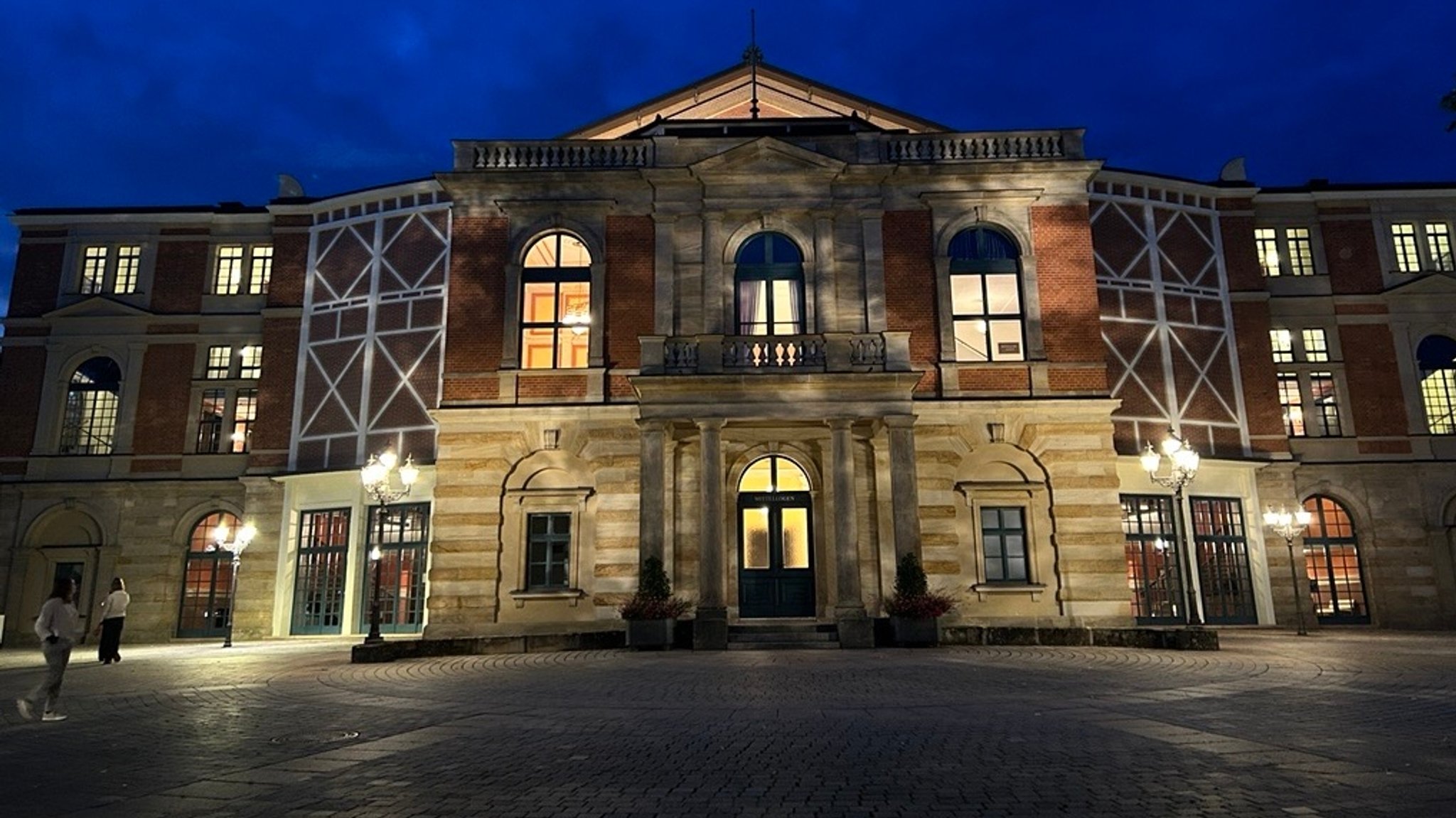 Blick auf das erleuchtete Bayreuther Festspielhaus bei Nacht.