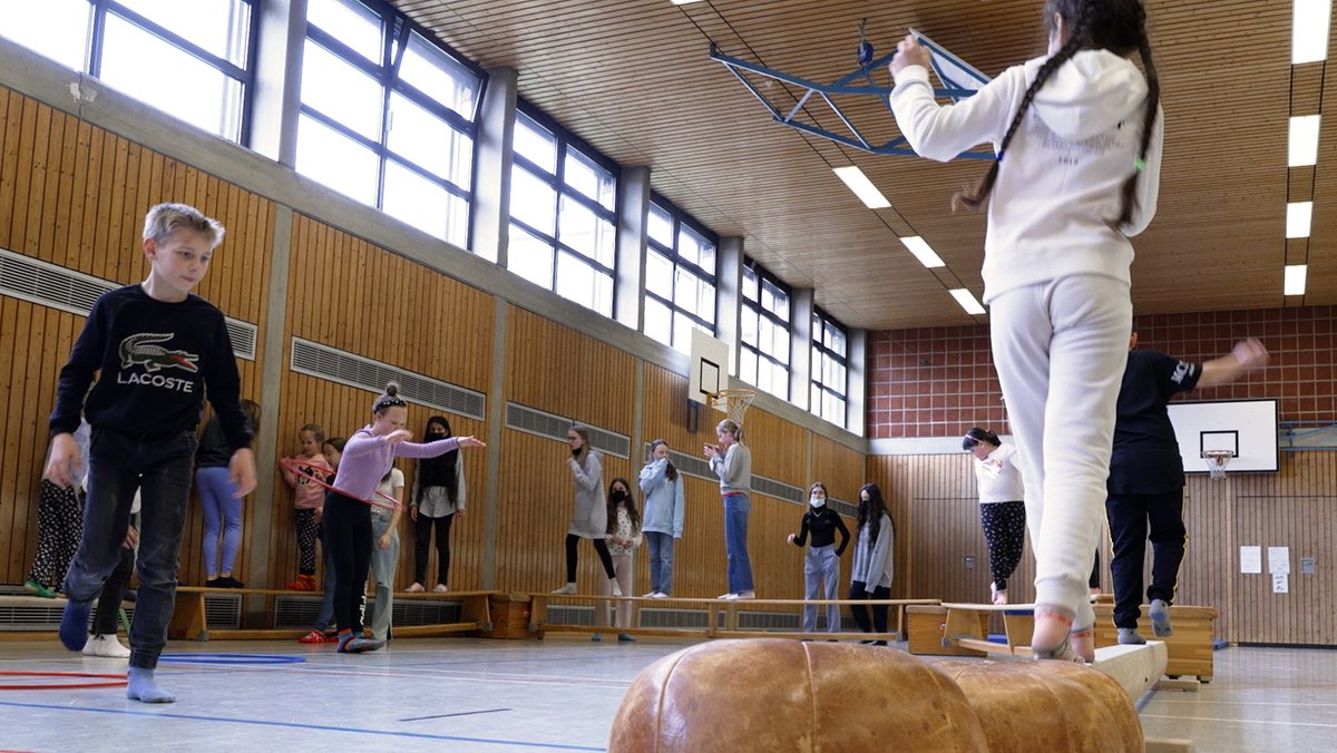 Blick in die Blick in die Turnhalle des Ignaz-Günther-Gymnasiums in Rosenheim. Kinder und Jugendliche balancieren auf einem Parcours aus Medizinbällen und Bänken.