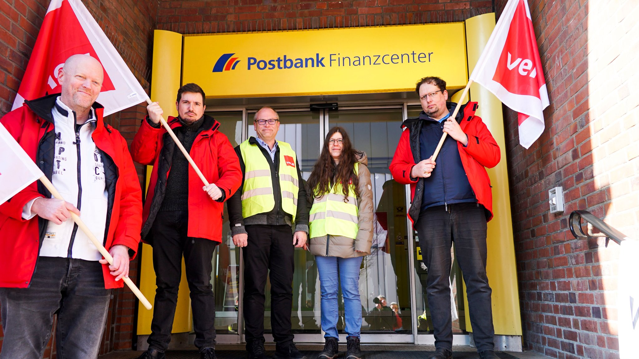 Beschäftigte mit Verdi-Fahnen vor einer geschlossenen Postbank Filiale