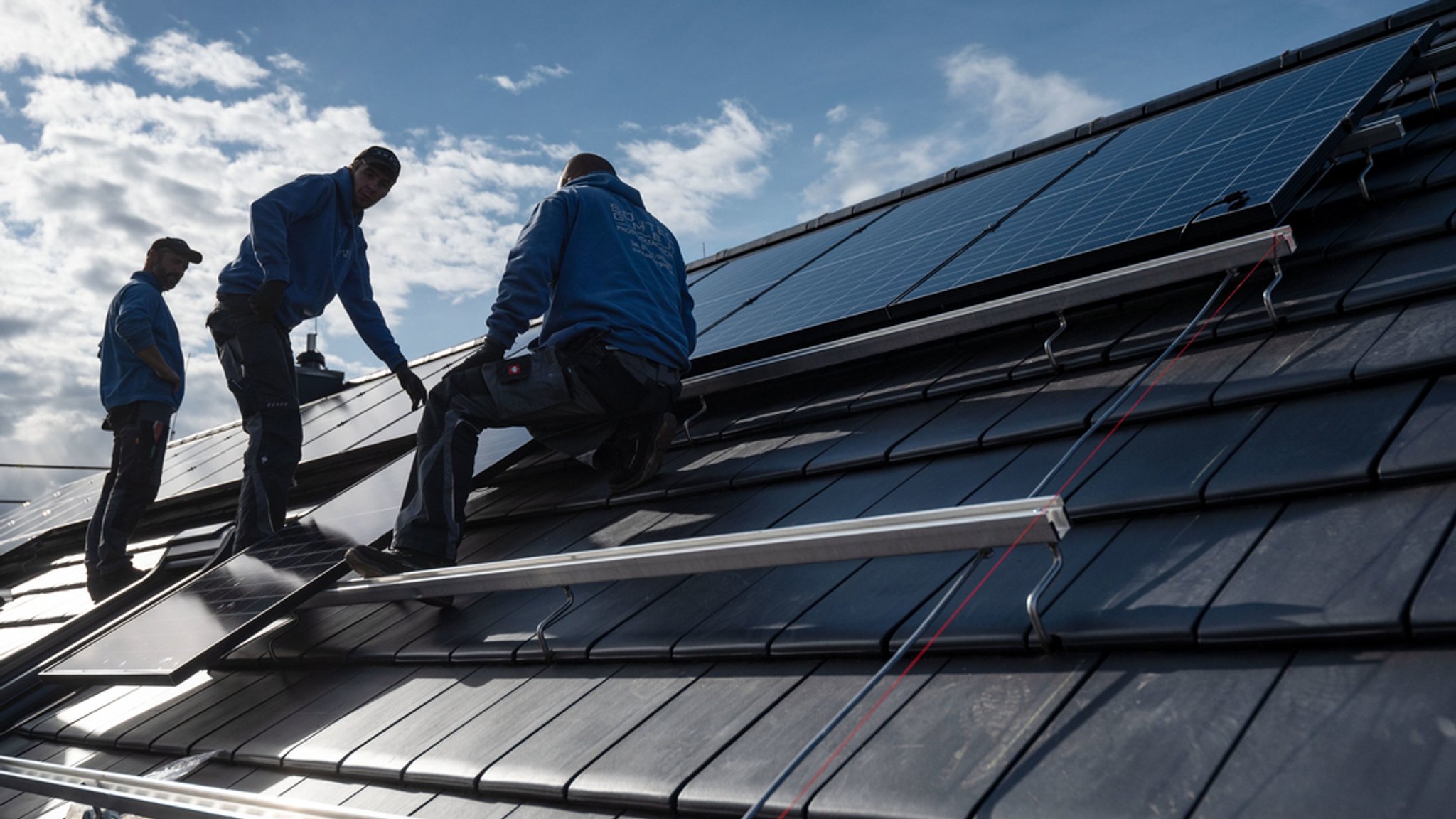 Drei Männer arbeiten an einer Solaranlage auf einem Dach.