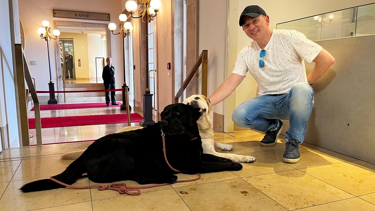 Ein schwarzer und wein weißer Hund zusammen mit einem Herrn, Intendant Joseph Köppliger im Foyer eines Theaters