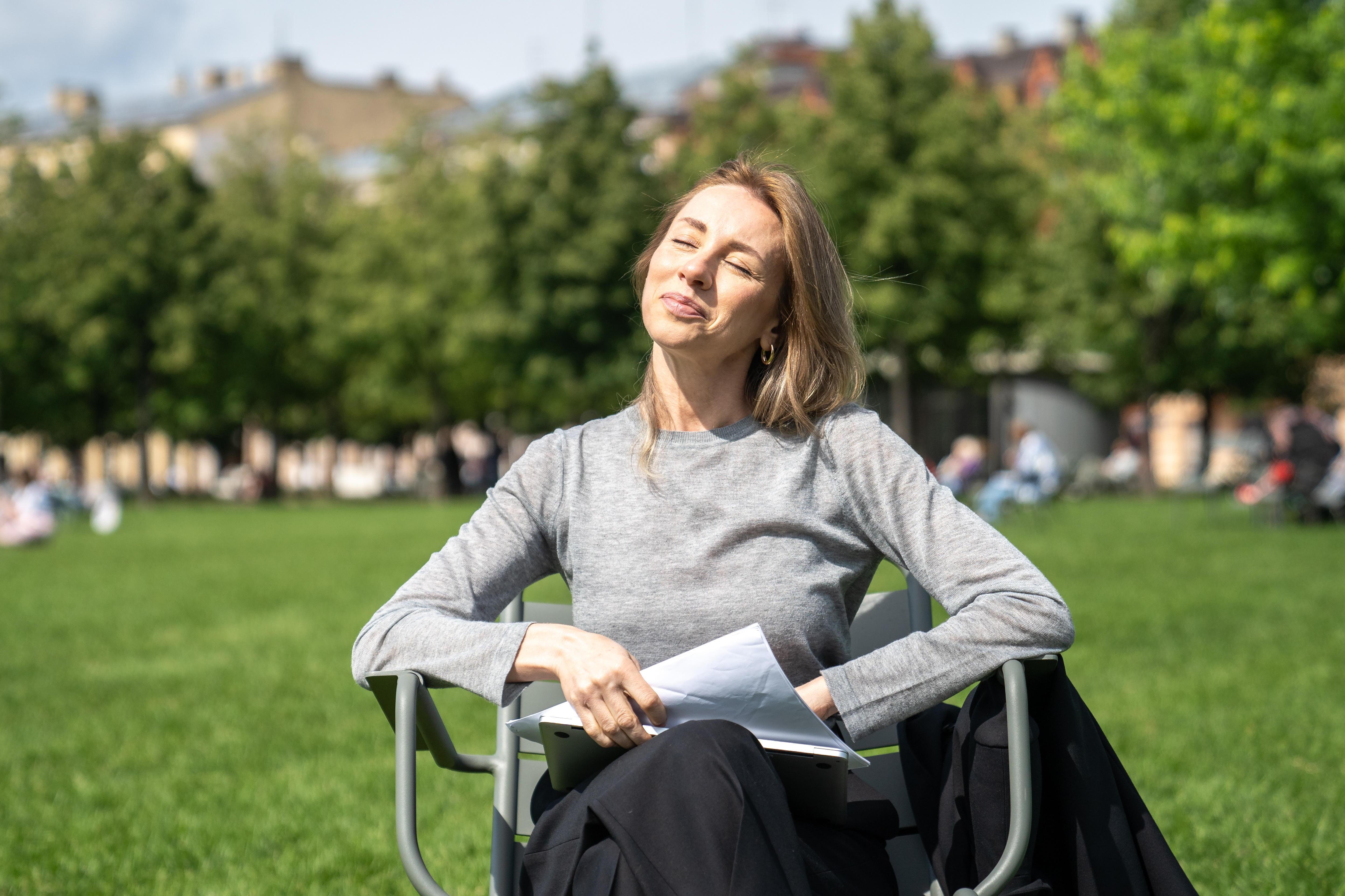 Frau sitzt auf einem Stuhl und hält ihr Gesicht in die Sonne