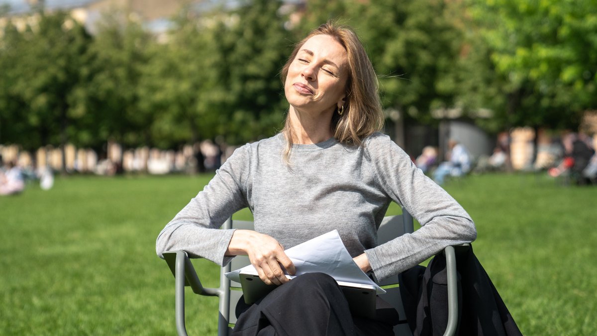 Frau sitzt auf einem Stuhl und hält ihr Gesicht in die Sonne