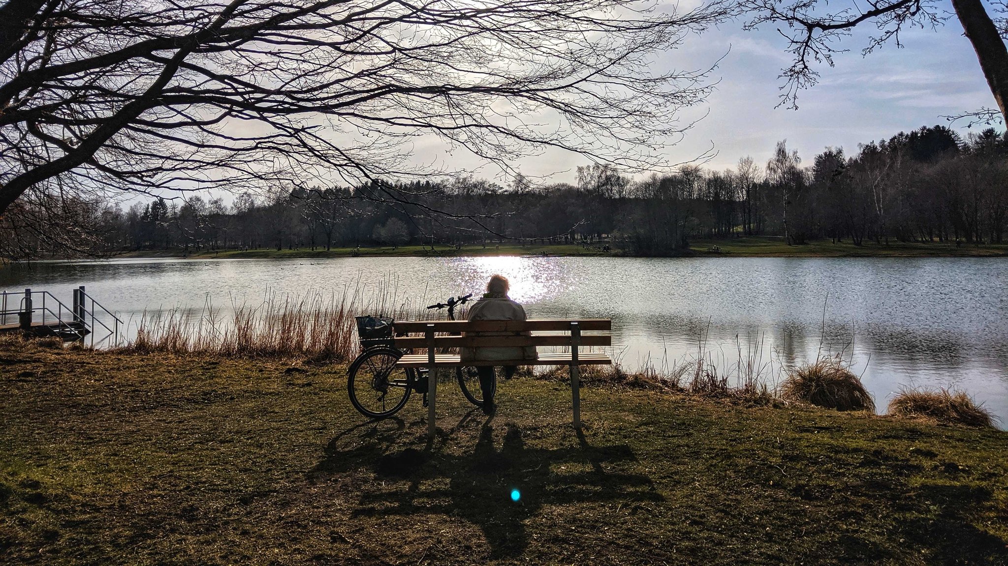 Frau sitzt auf einer Parkbank an einem kleinen See (Aufnahme vom 10.04.2020)