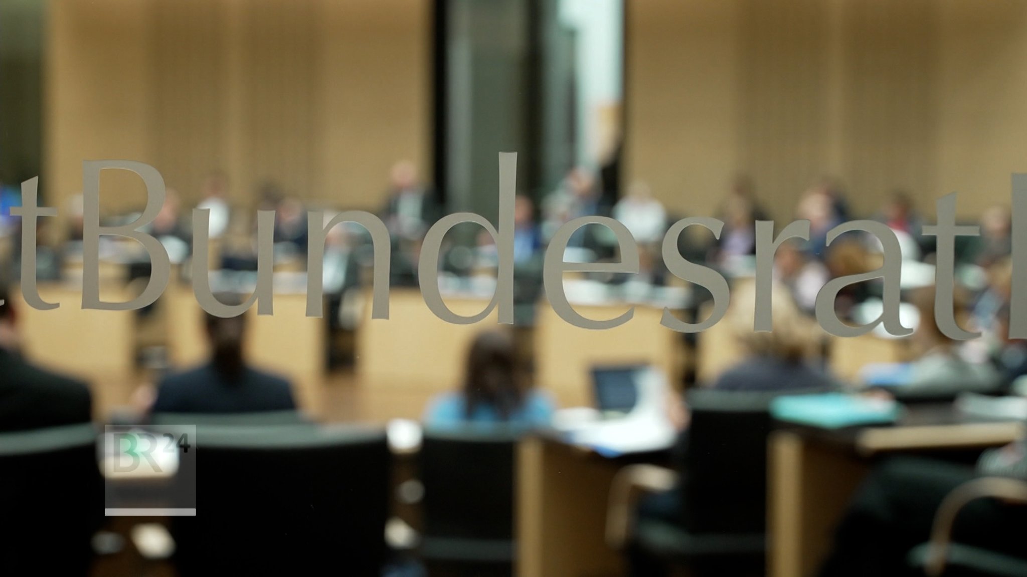 Schriftzug "Bundesrat" auf einer Glastür, dahinter eine Bundesratssitzung