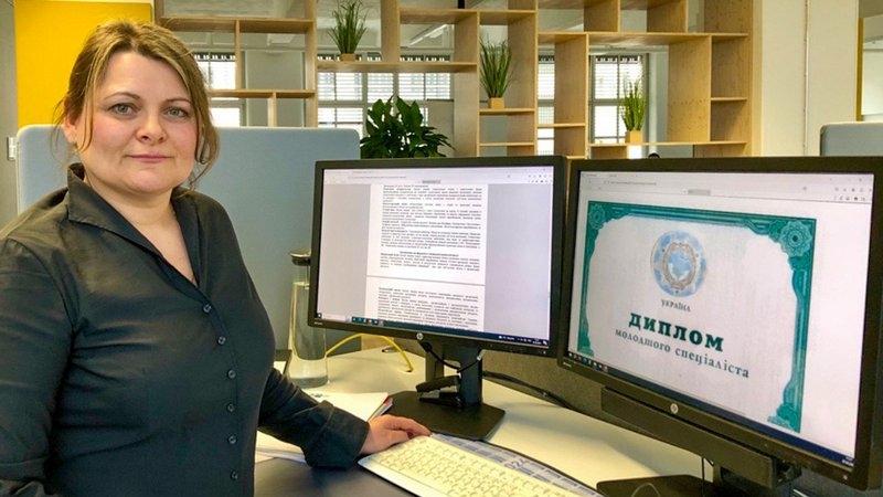 Frau steht vor zwei Monitoren in einem Büro.