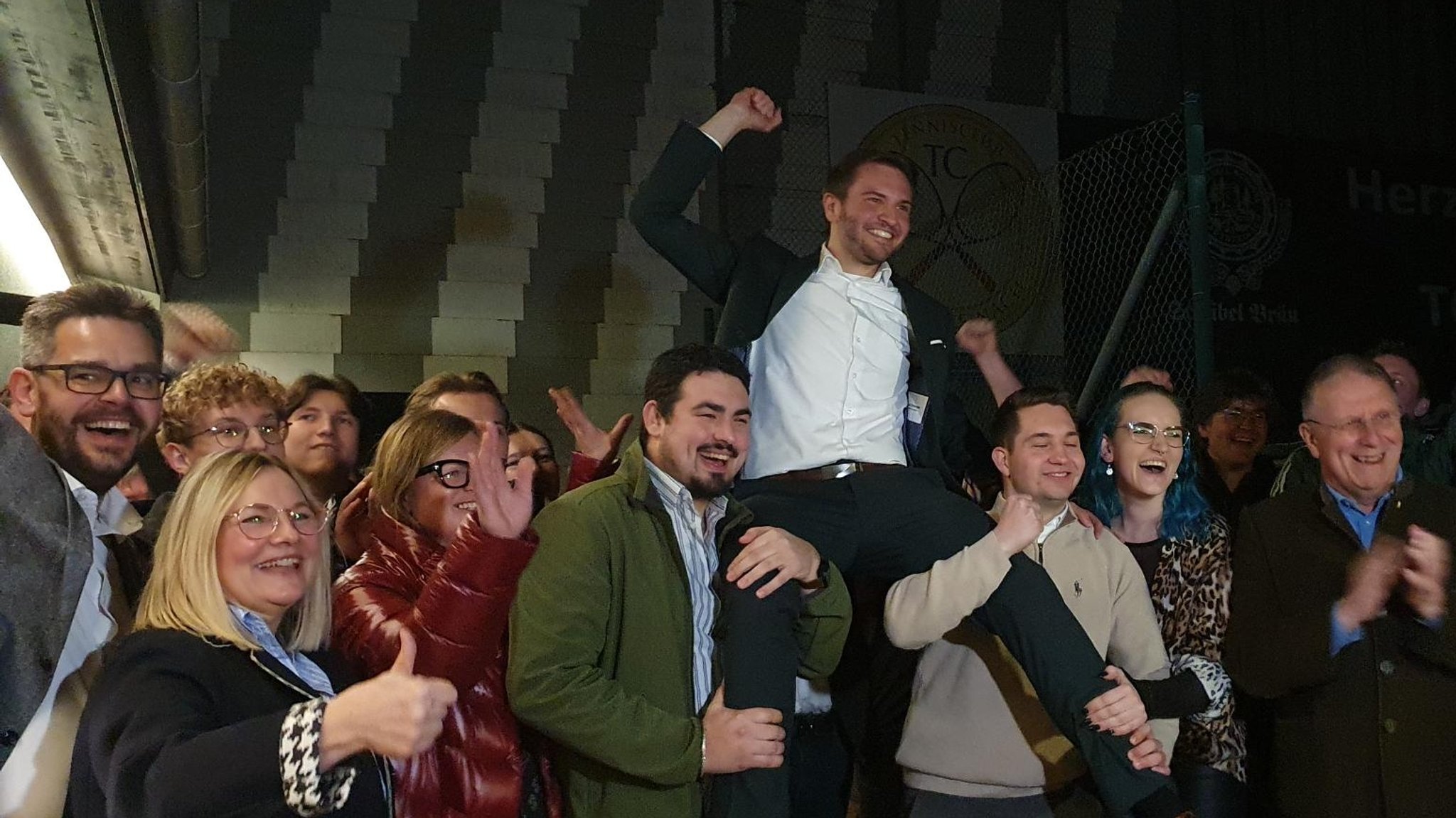 Feiernde Menschen halten einen jubelnden Mann auf ihren Schultern. 