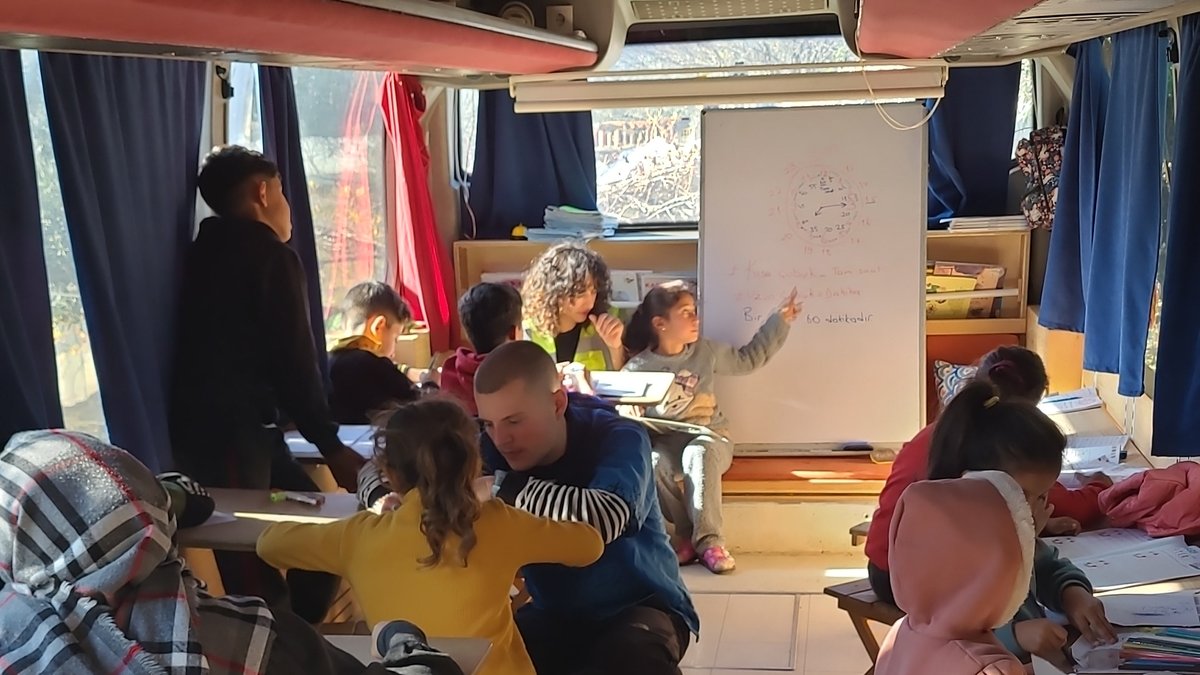 Zu sehen sind Kinder, die in dem umgebauten Bus an kleinen Bänken lernen.