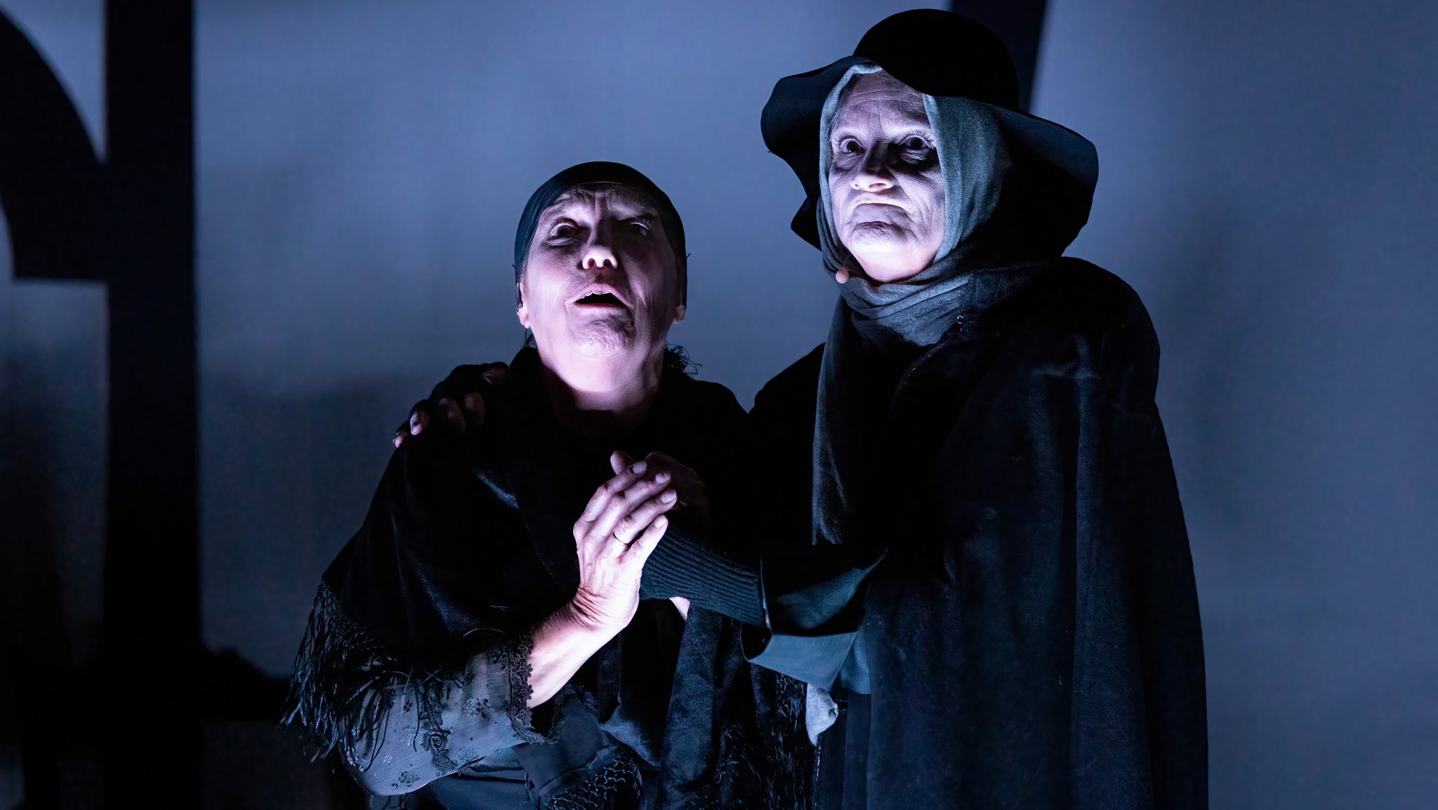 Eine Frau und ein Mann stehen in dunklen Kostümen vor einer grauen Bühnenwand ("Der Brandner Kaspar" am Landestheater Oberpfalz)