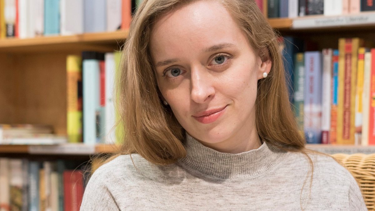 Autorin Alina Herbing blickt vor einer Bücherwand lächelnd in die Kamera