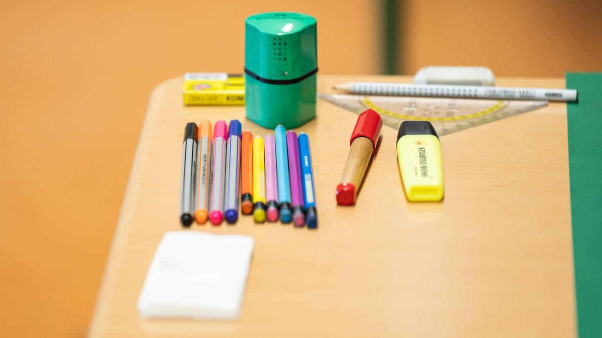 Verschiedene Stifte und Utensilien liegen auf einem Tisch in einem Klassenzimmer