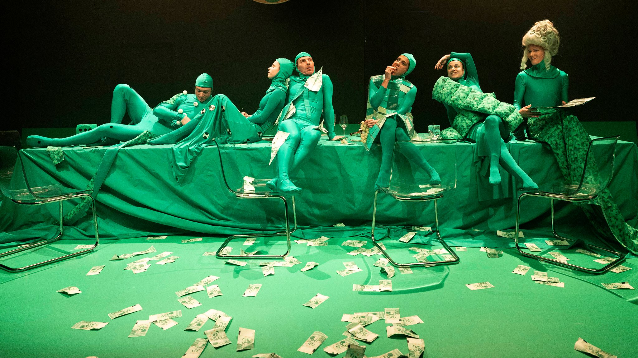 Die Mitwirkenden in grünen Kostümen auf einem Tisch sitzend