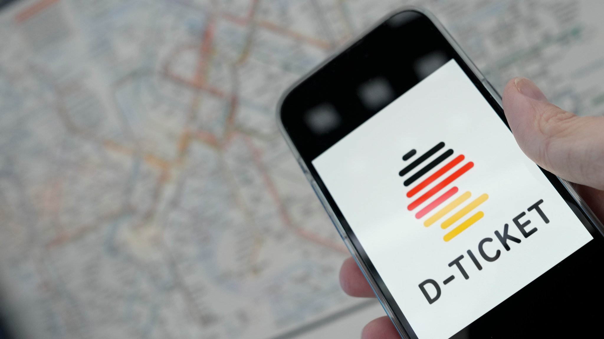 Deutschlandticket-Logo auf einem Smartphone, im Hintergrund ein Fahrplan