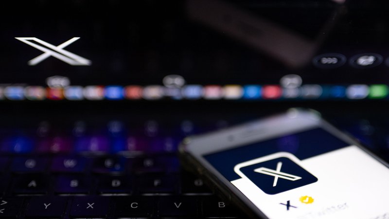 Auf dem offiziellen Profil der Plattform X auf dem Bildschirm eines Smartphones und auf dem Display eines Laptops ist der weiße Buchstabe X auf schwarzem Hintergrund zu sehen. 
