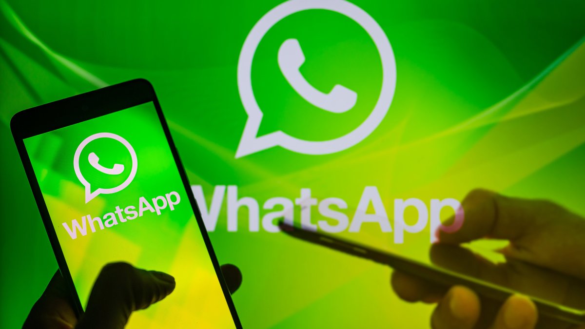 Das WhatsApp-Logo im Hintergrund und auf einem Smartphone-Display, eine andere Hand hält ein weiteres Smartphone.