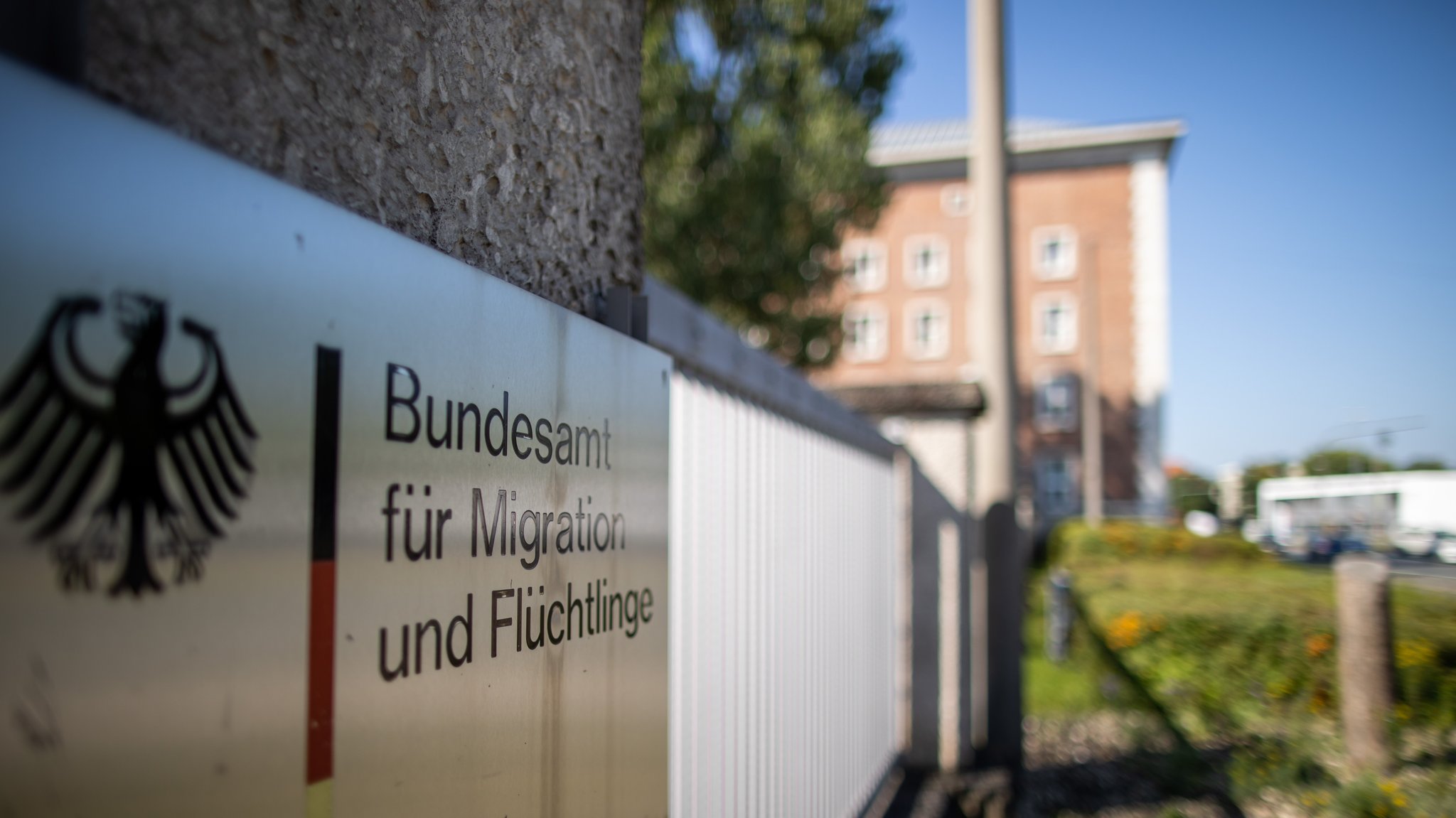 Schild mit der Aufschrift "Bundesamt für Migration und Flüchtlinge", dahinter das Amtsgebäude.