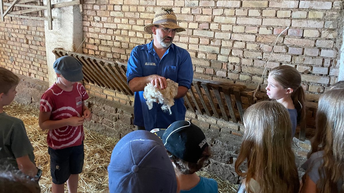 Landwirt Martin Eck zeigt den Fünftklässlern echte Schafwolle.