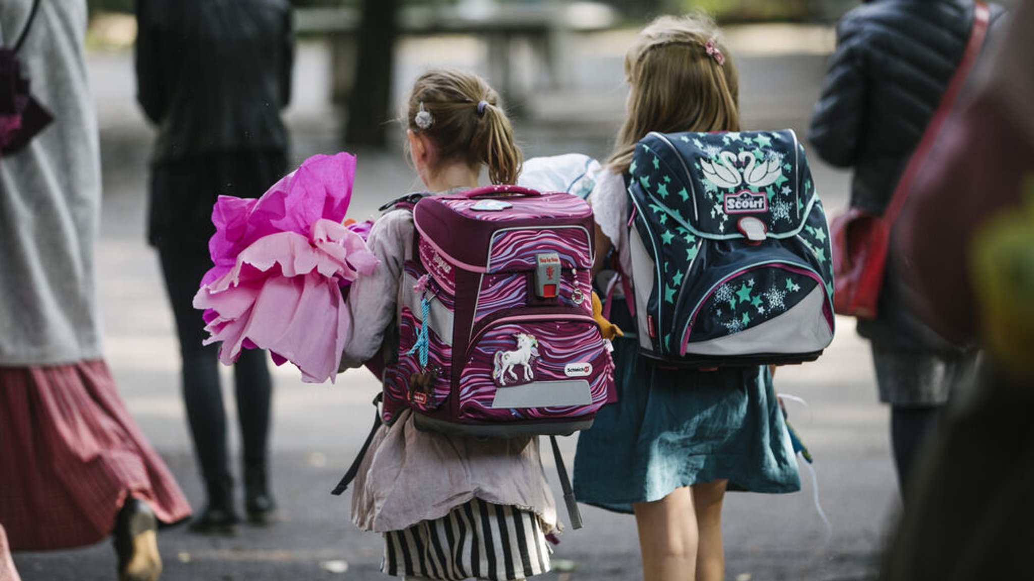 Zwei Mädchen laufen bepackt mit Rucksack und Schultüte nebeneinander her.