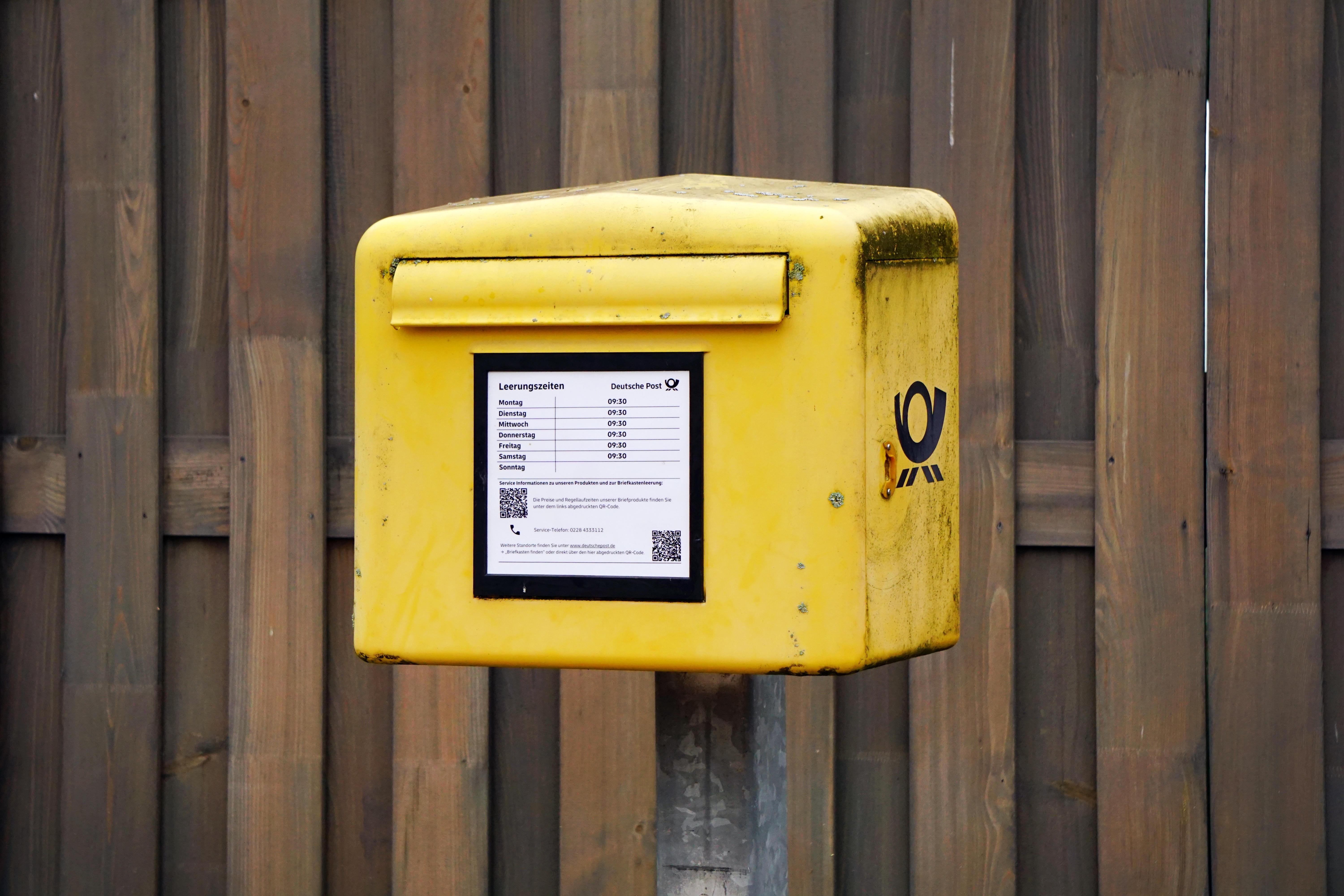 gelber Briefkasten der Deutschen Post mit deutlichen Gebrauchsspuren an einer Holzwand
