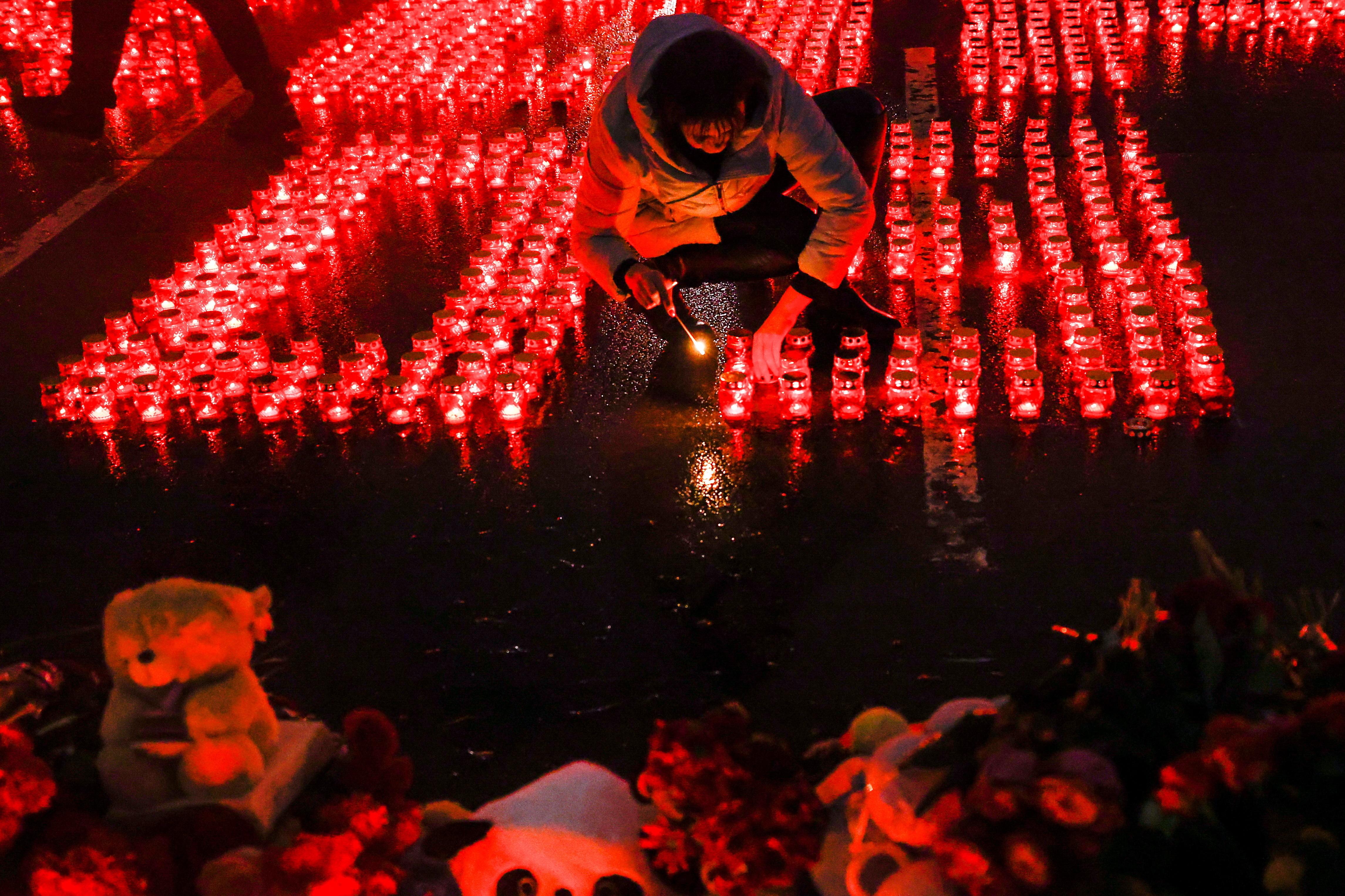 Eine Passantin entzündet eine Kerze inmitten vieler weiterer Grabkerzen.