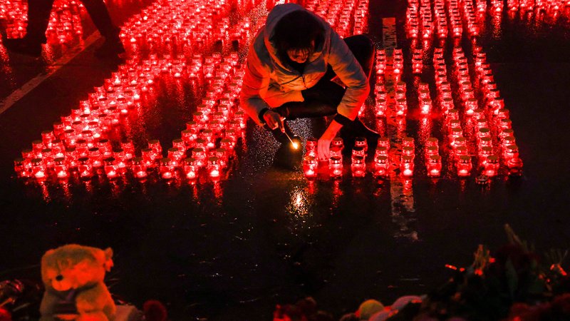 Eine Passantin entzündet eine Kerze inmitten vieler weiterer Grabkerzen.