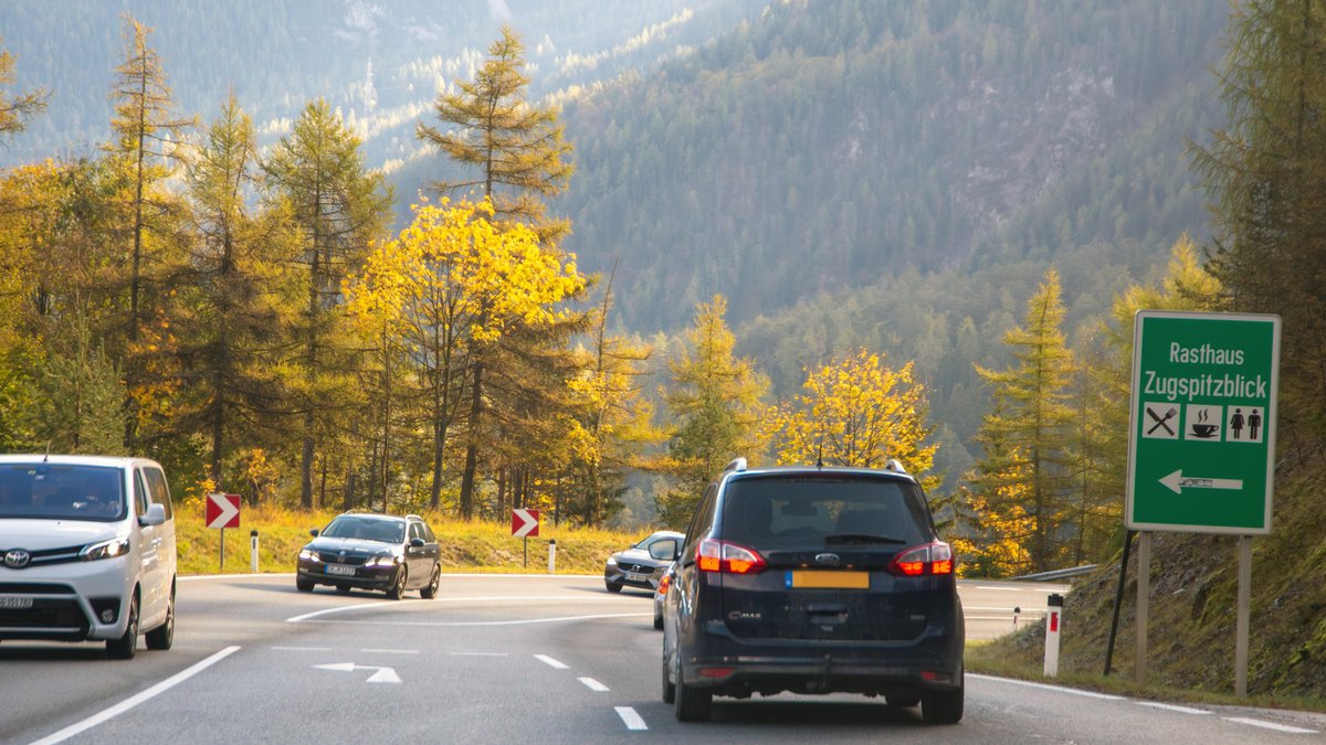 Autos fahren auf der Straße, der über den Fernpass in Tirol führt. Im Hintergrund bewaldete Berghänge.