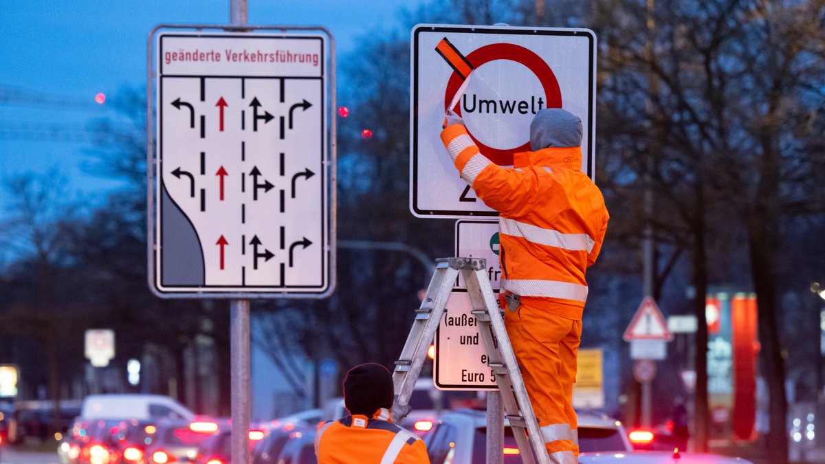 Arbeiter entfernen einen roten Klebestreifen von einem Schild mit der Aufschrift «Umwelt Zone» und «Diesel»