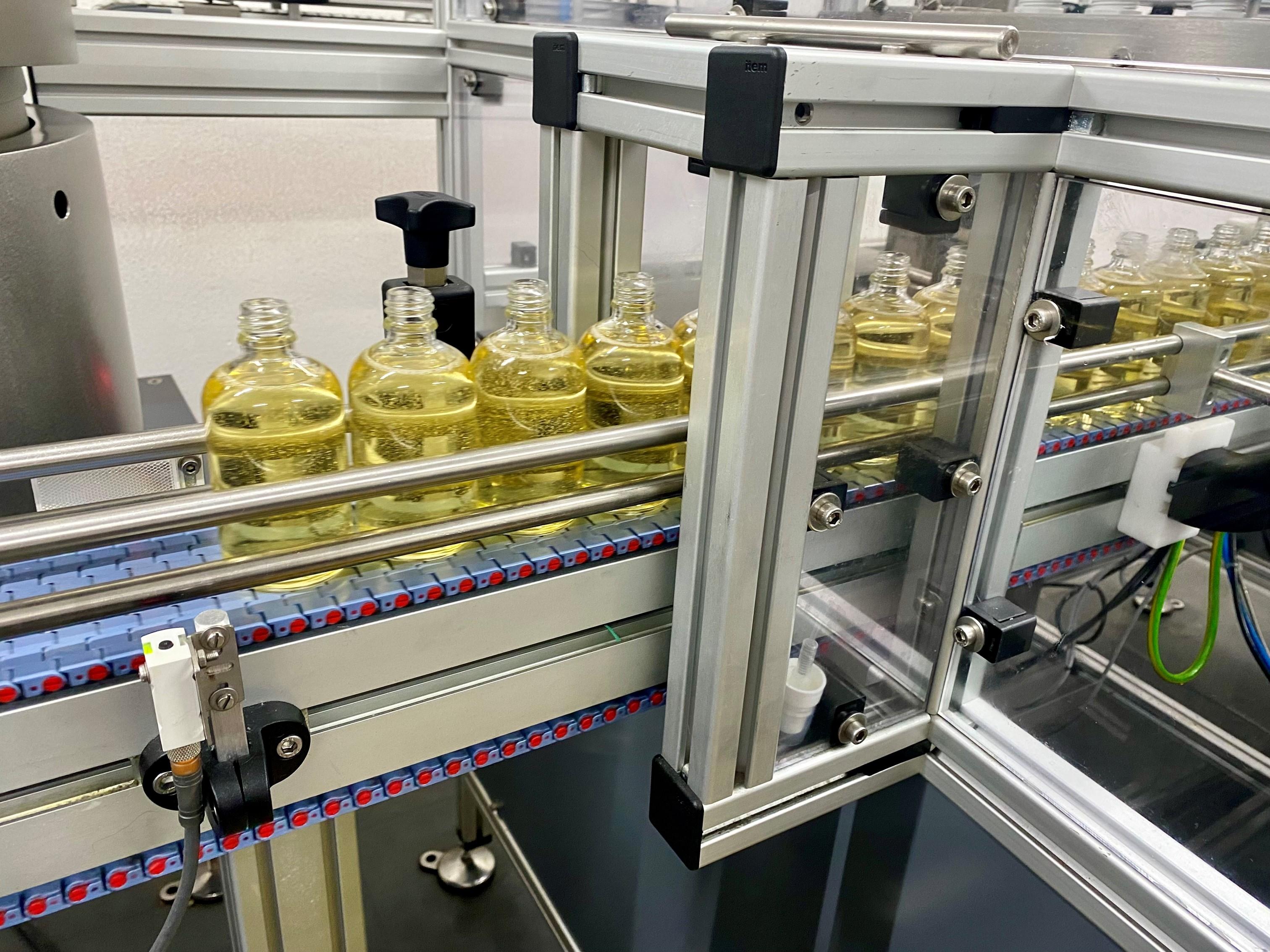 Mehrere Flaschen mit einer gelblichen Flüssigkeit auf einem Fließband.
