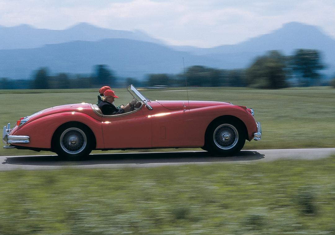 Ein älteres Paar fährt mit einem Cabrio in Berglandschaft - Symbolbild 