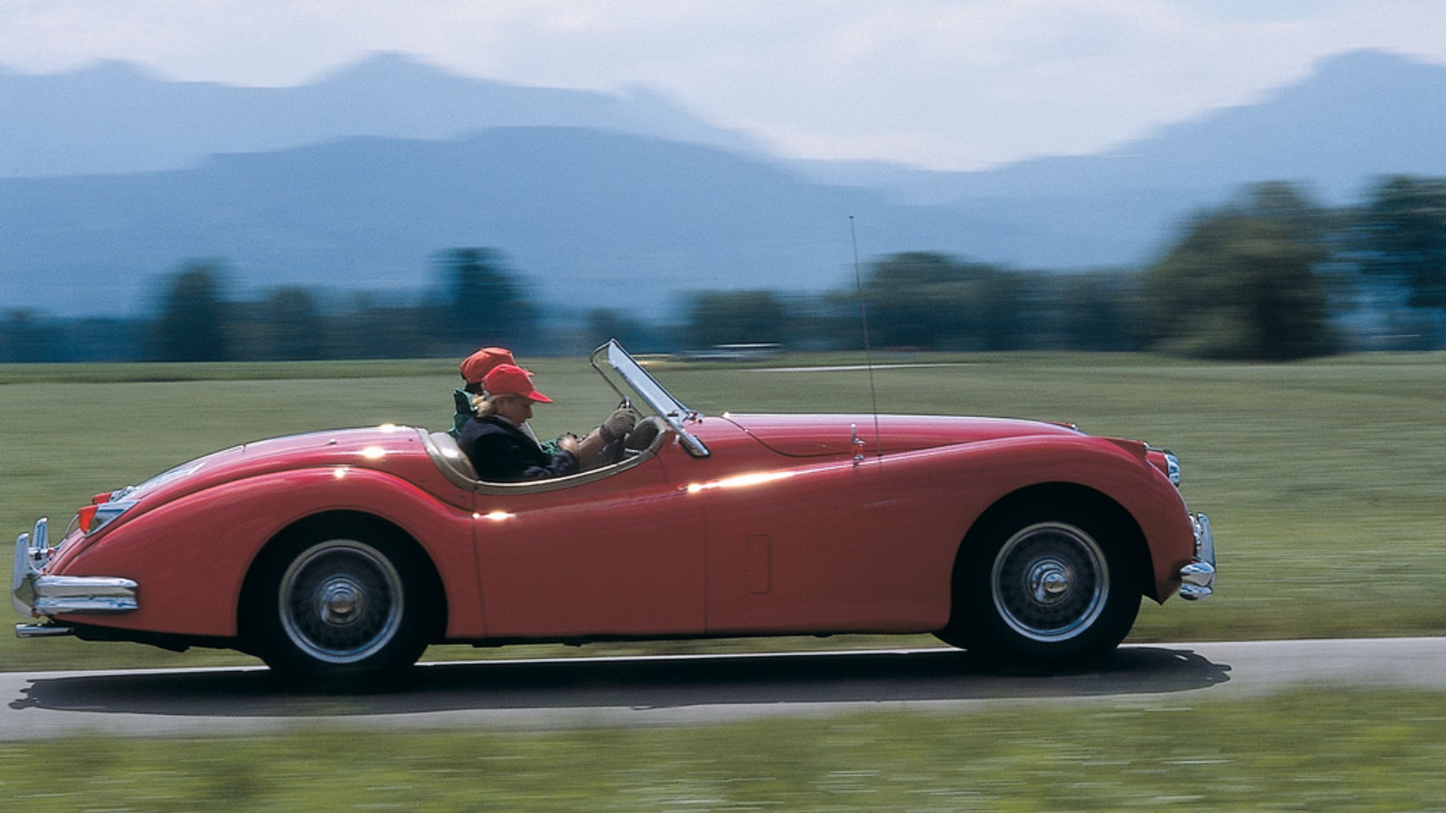 Ein älteres Paar fährt mit einem Cabrio in Berglandschaft - Symbolbild 