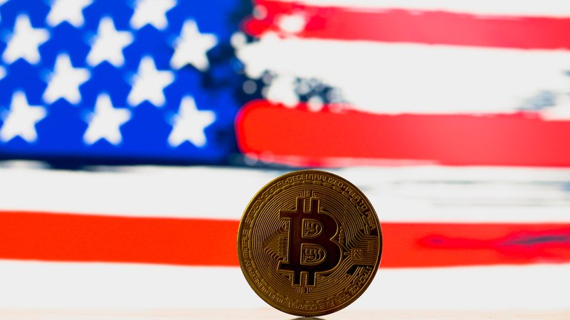 Bitcoin-Münze vor US-Flagge | Bild: picture alliance / Sipa Bitcoin-Münze vor US-Flagge