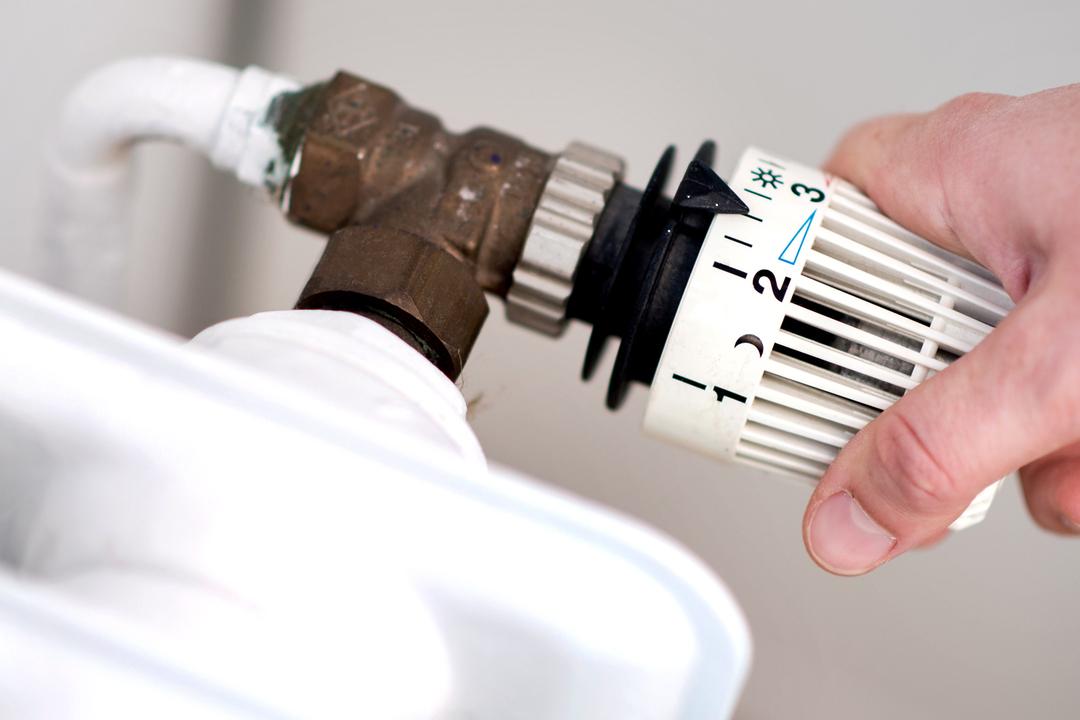 Hand an einem Heizungsthermostat.
