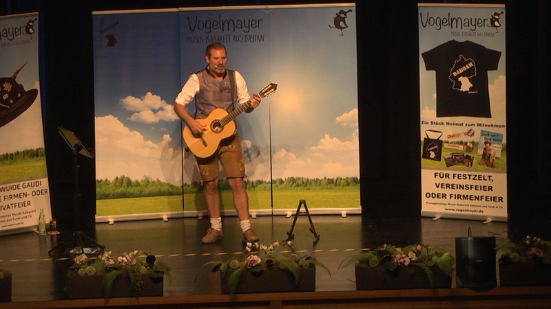 Thomas Mayer steht mit Gitarre auf einer Bühne.