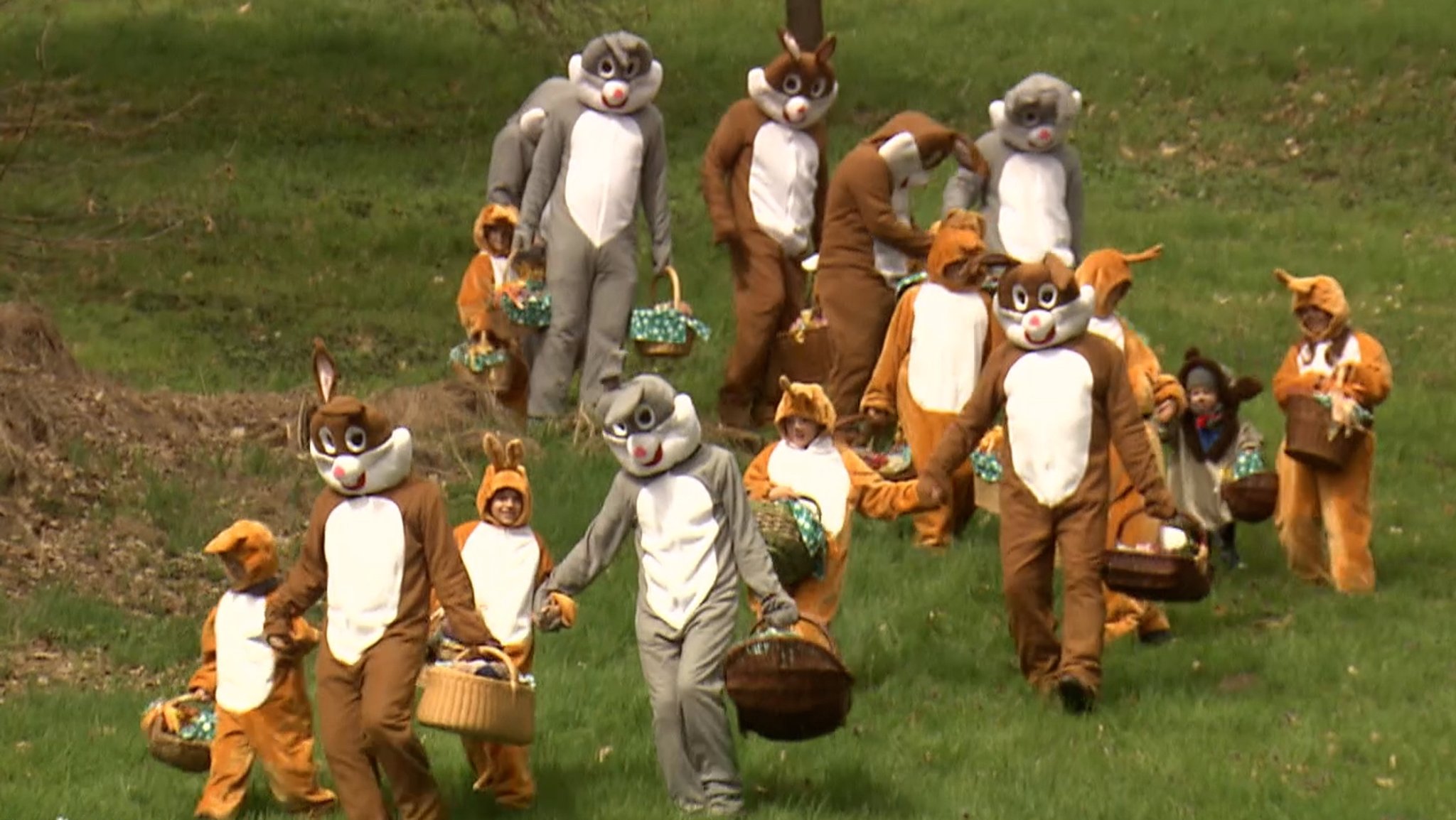 Kinder und Erwachsen sind als Osterhasen verkleidet und marschieren über eine Wiese. 