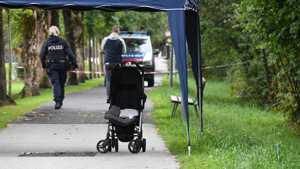 28.08.2022, Österreich, St. Johann in Tirol: Polizisten ermitteln an einem Abgesperrten Bereich eines Gehwegs, auf dem eine Kinderkarre steht.