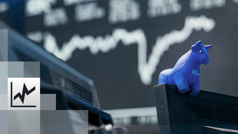 Ein blauer Stier aus Gummi sitzt auf der oberen Kante eines Bildschirmes. Im Hintergrund die Kurstafel der Börse