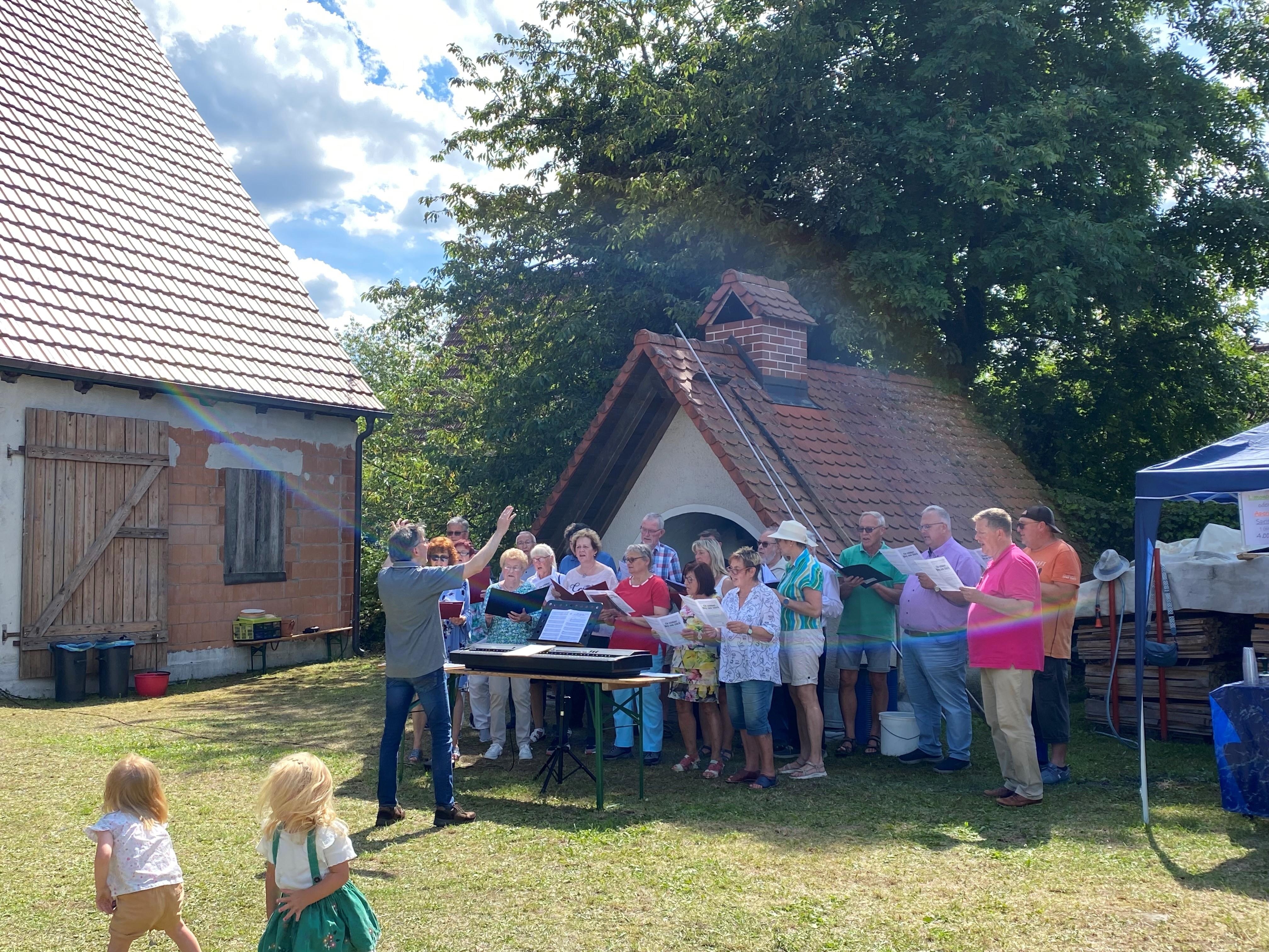 Singende Menschen stehen vor einem alten Backofen. 