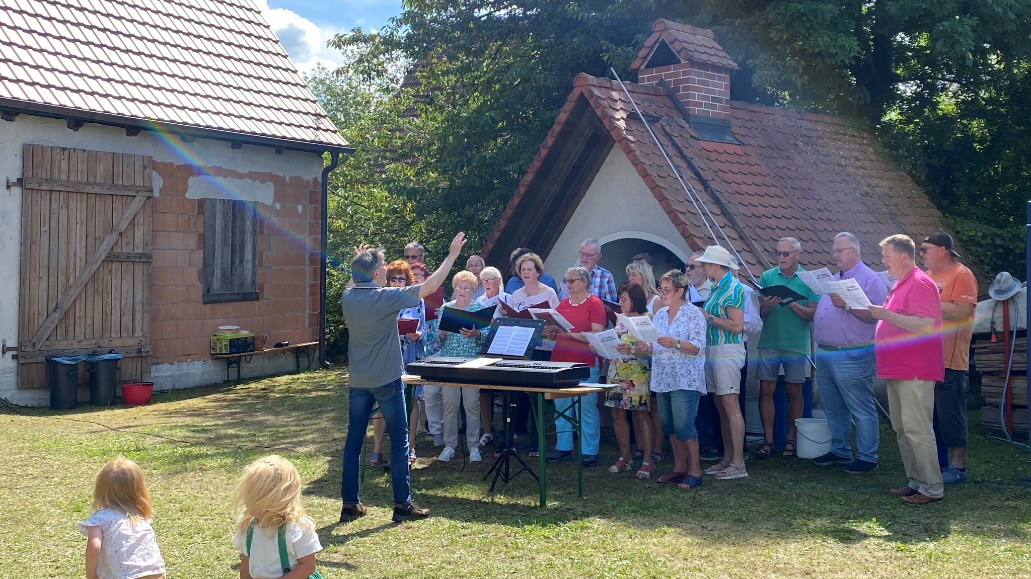 Singende Menschen stehen vor einem alten Backofen. 