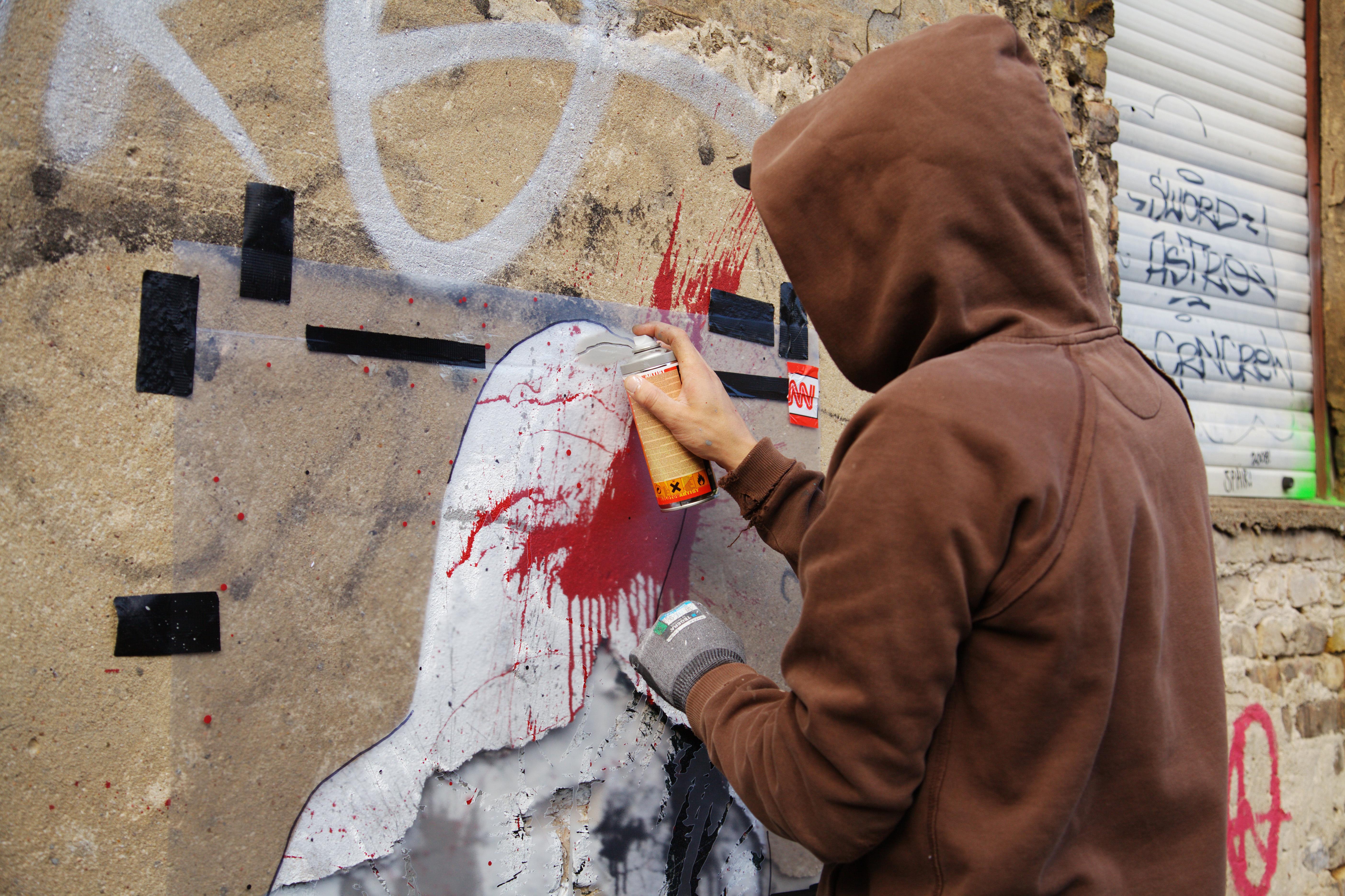 Ein Unbekannter sprüht mit einer Spraydose Farbe auf eine Wand.