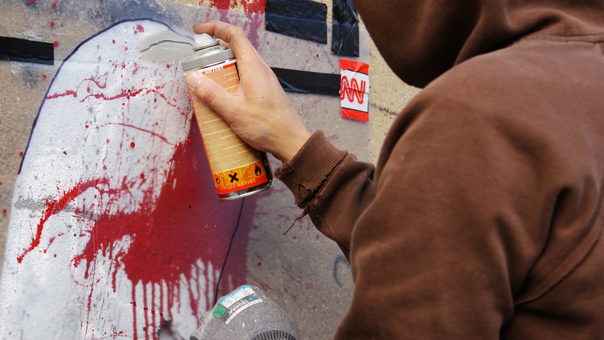 Ein Unbekannter sprüht mit einer Spraydose Farbe auf eine Wand.
