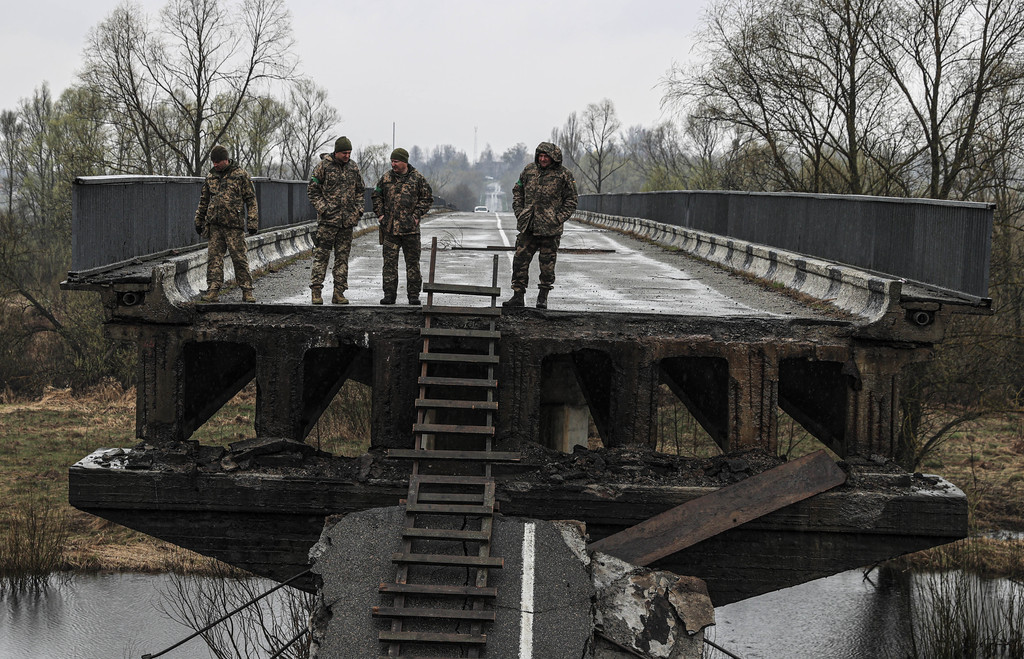 Männer im Kampfanzug stehen auf den Resten einer eingestürzten Brücke