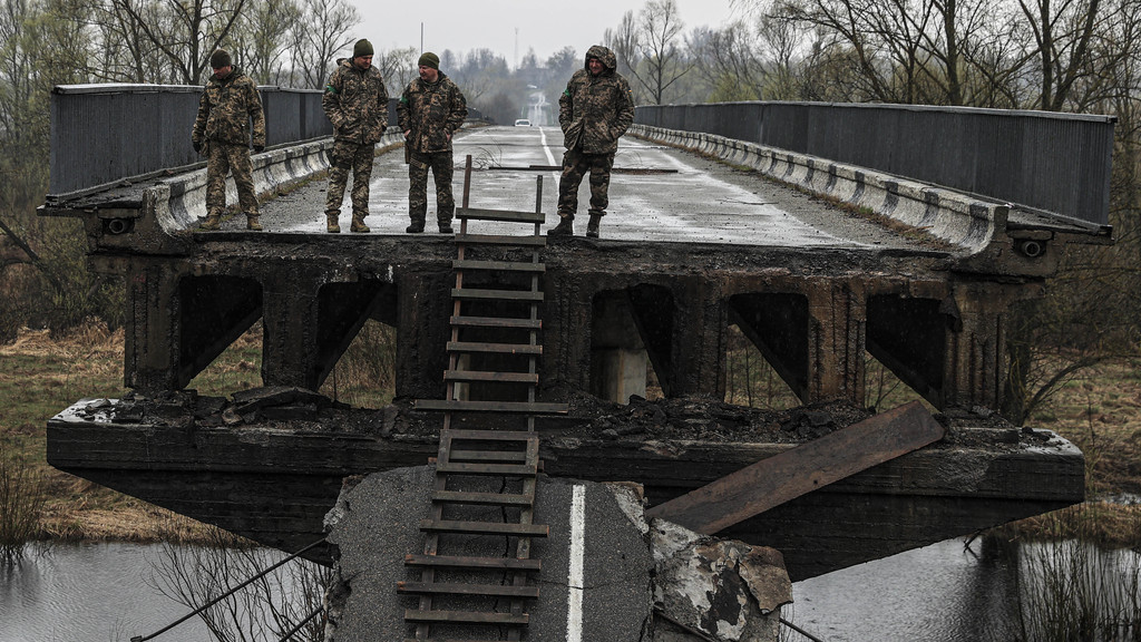 Männer im Kampfanzug stehen auf den Resten einer eingestürzten Brücke