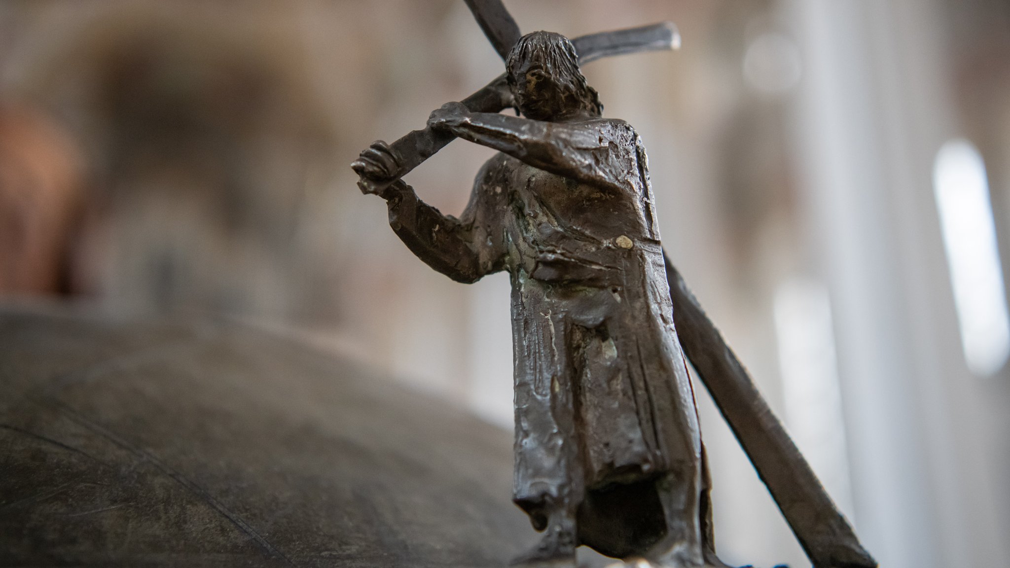 Eine Bronzefigur, die Jesus zeigt, wie er das Kreuz trägt, steht in der Münchner Heilig Geist-Kirche am Taufbecken.