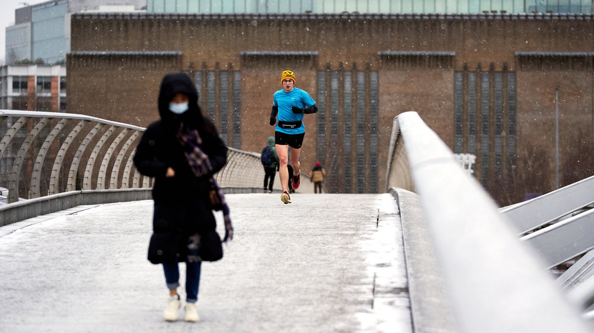 Ein Läufer überquert bei Schneefall die Millennium Bridge in London.