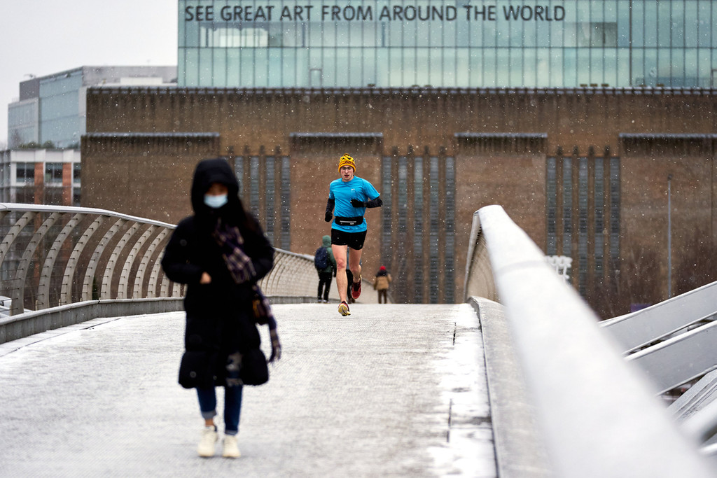 Ein Läufer überquert bei Schneefall die Millennium Bridge in London.