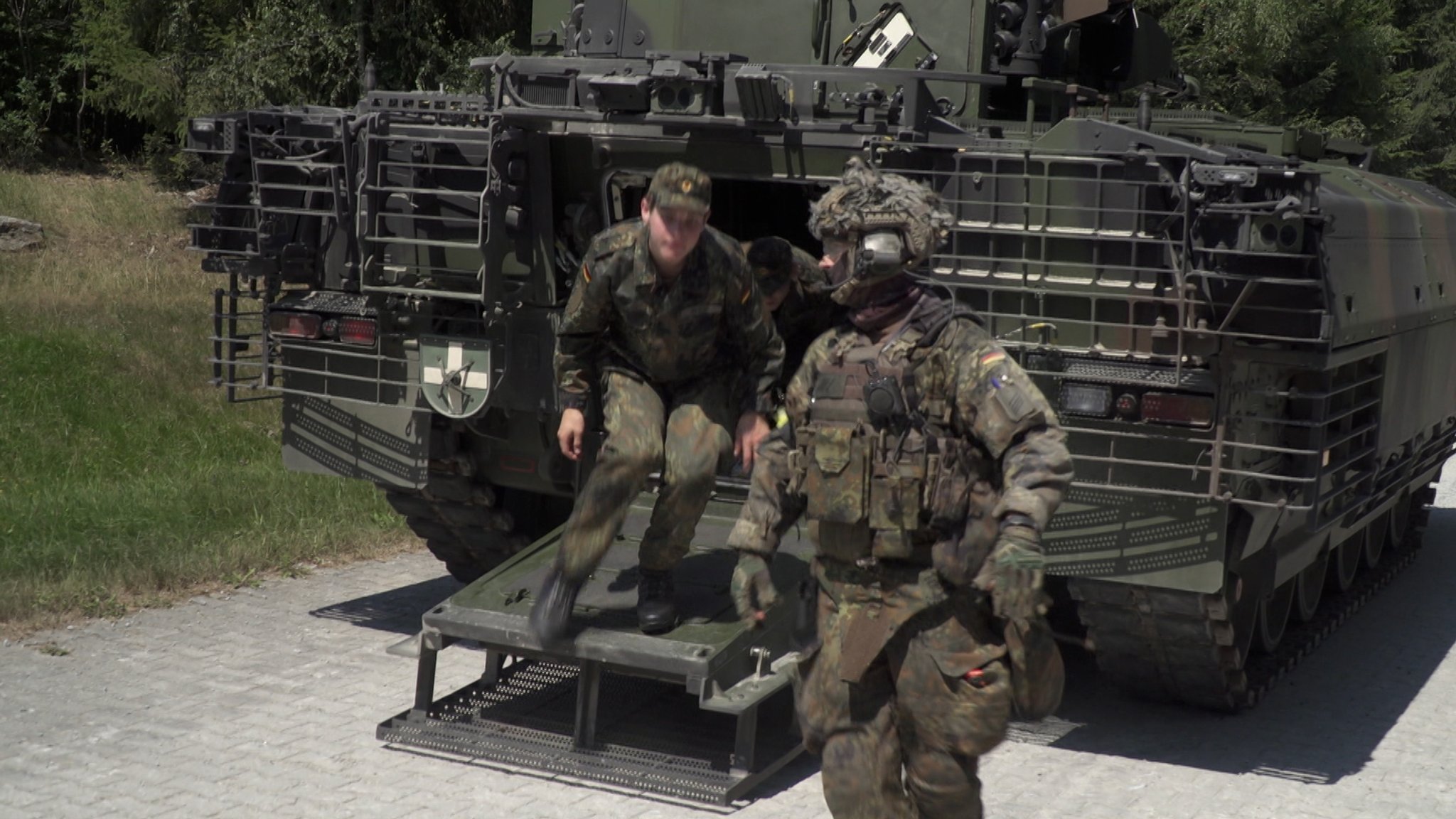 Zwei Personen in voller Ausrüstung vor einem Panzer.