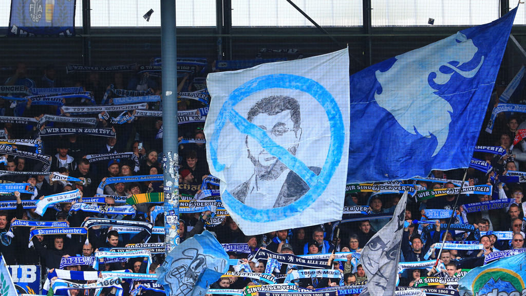 Fans des TSV 1860 München schwenken eine Fahne mit dem durchgestrichenen Gesicht von Hasan Ismaik