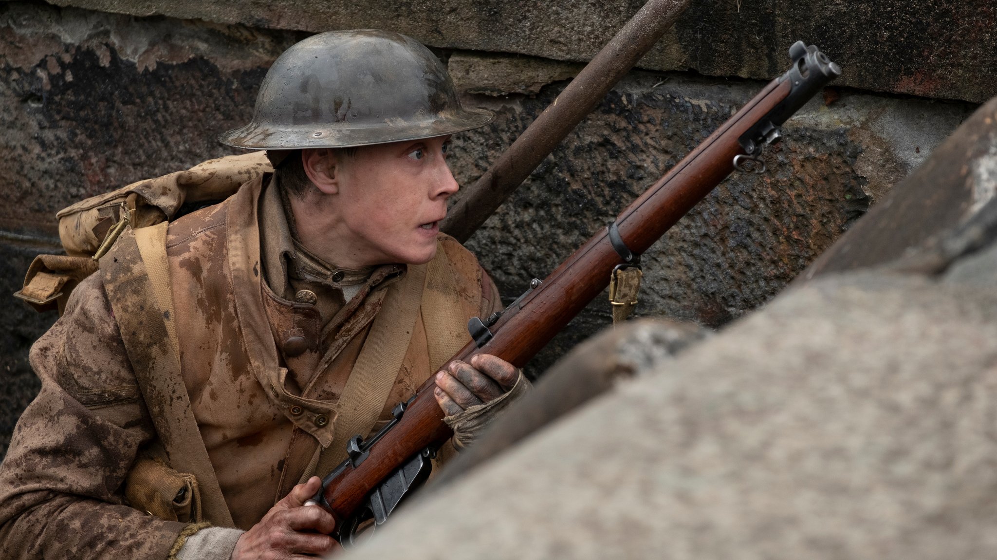 Soldat mit Gewehr und Stahlhelm, vor eine Mauer geduckt (Filmszene)