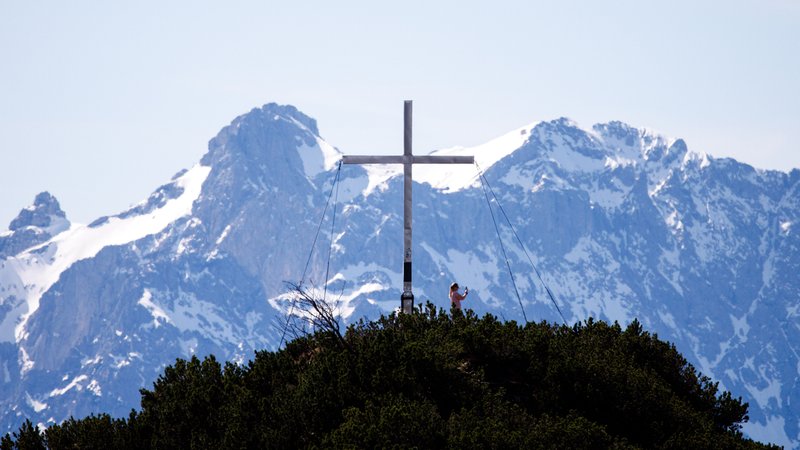 ARCHIV: Eine Auflüglerin steht am 14.04.2024 am Gipfel vom Martinskopf in der Nähe vom Herzogstand bei Urfeld (Bayern) und nimmt ein Foto vom Bergpanorama auf.