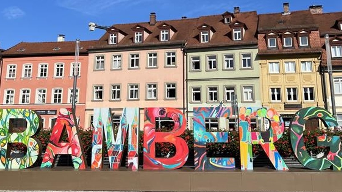 In bunten Buchstaben stehen Bamberg-Buchstaben als Fotomotiv in der Stadt. Im Hintergrund sind Pflanzen und Häuser zu sehen.